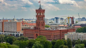 Rotes Rathaus steht in einer städtischen Umgebung mit Wolken.