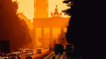 Brandenburger Tor silhouettiert, Autos fahren bei Sonnenuntergang.