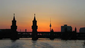 Brücke mit Türmen, silhouettiert gegen Sonnenuntergang über Wasser.