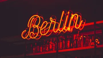Neon-Schriftzug `Berlin` leuchtet über einer Regale mit Flaschen.