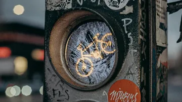 Traffic light shows a bicycle symbol surrounded by city graffiti.