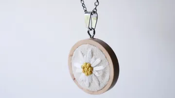 Necklace holds round pendant with embroidered floral motifs.