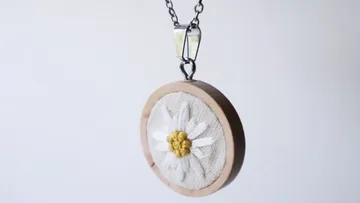 Ein runder Anhänger zeigt eine gestickte Blume, schwebend.