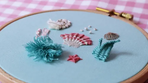 Gestickte Muscheln und Meerestiere auf blauem Stoffrahmen.