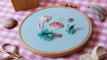 Gestickte Muscheln und Seesterne auf blauem Stoffrahmen.