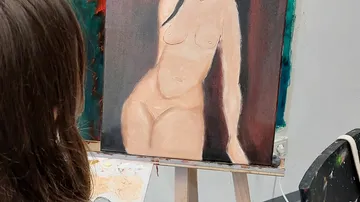 Künstlerin malt nacktes Modell in einem Studio.