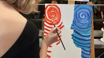Eine Person malt mit Pinsel Spiralen auf Leinwand.