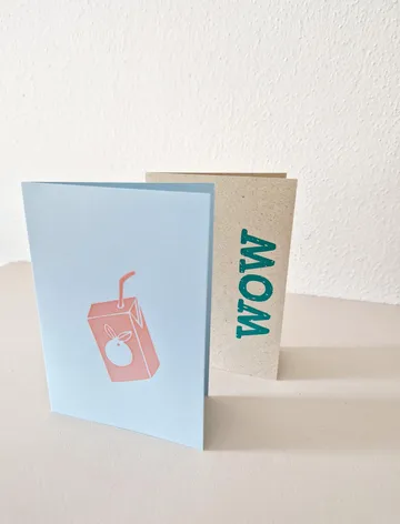 Zwei Karten stehen auf einem Tisch, eine mit Saftpackung.