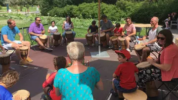 Menschen sitzen und spielen Trommeln in einem Park.