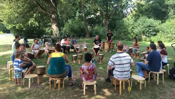 Menschen sitzen im Kreis und spielen auf Trommeln im Park.