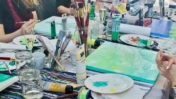 Farben und Pinsel liegen auf einem kreativen Tisch.