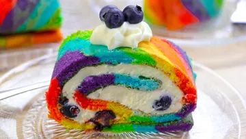 Bunte Regenbogenrolle mit Sahne und Blaubeeren auf Dessertteller.