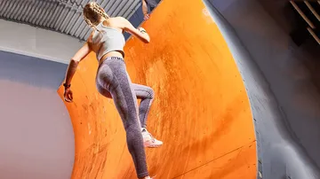 A person climbs up an orange sports wall.