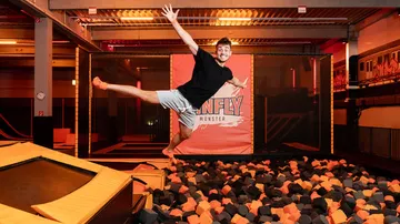 Young man jumps into a foam ditch in a trampoline arena.