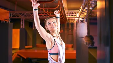 Sportlerin hangend, lächelt in modernem Trainingsbereich.