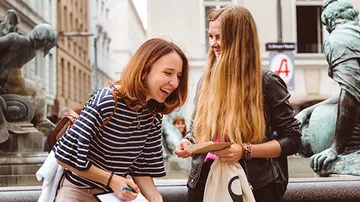 Two girls laugh and talk in front of a statue.