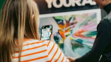 Frau macht Foto einer bunten, abstrakten Kunst mit Smartphone.