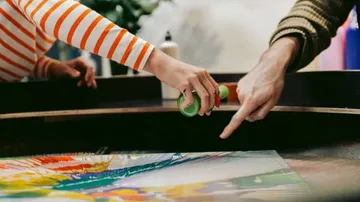 Hands spray paint on a work of art in a studio.