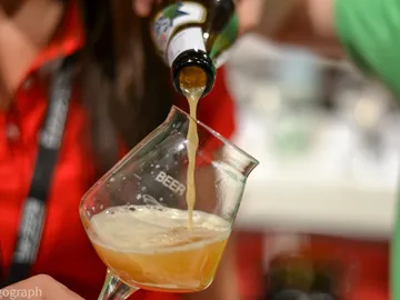 Ein Glas wird mit Bier gefüllt, umgeben von Menschen.