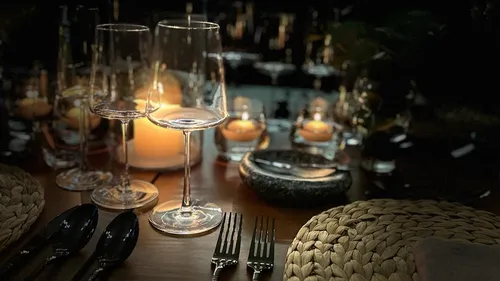 Zwei Gläser stehen auf einem gedeckten Tisch bei Kerzenlicht.
