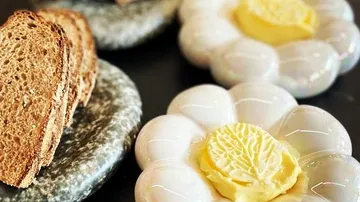 Scheiben Brot liegen neben kunstvollen Butterplätzchen auf Tellern.