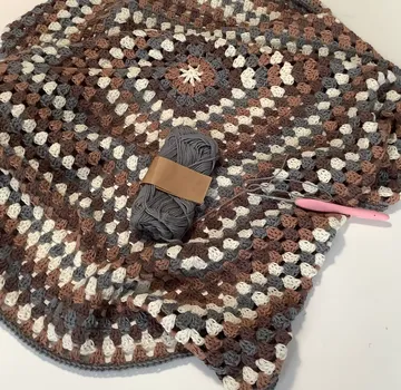 Gestrickter Teppich liegt daneben, graues Garn und Häkelnadel.