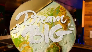 Spiegel zeigt „Dream Big“ über einer Weltkarte.
