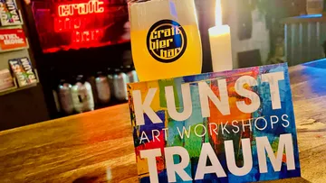 Glas mit Bier steht neben einer Kerze und Kunstkarte.
