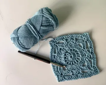 Hellblaues Garn liegt neben einem gehäkelten Quadrat.