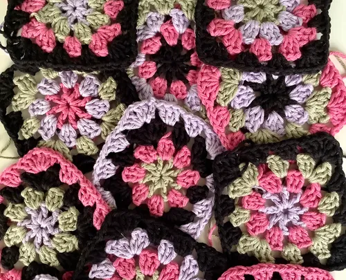 Colored crocheted squares lie on top of each other on a surface.