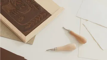 Linoleumplatte mit Zeichen, Werkzeuge liegen daneben, Arbeitsbereich.