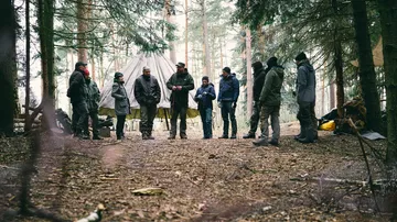 Eine Gruppe von Personen steht im Wald und diskutiert.