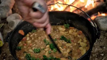 Ein Topf mit Eintopf wird am Feuer gerührt.