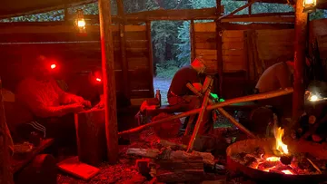 Holzarbeiter schnitzen im schwachen Licht einer Lagerfeuerstätte.