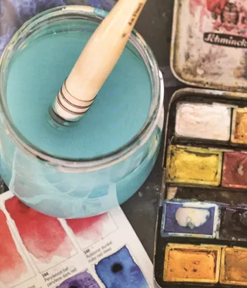 Ein Pinsel ist in blauer Farbe in einem Glas.