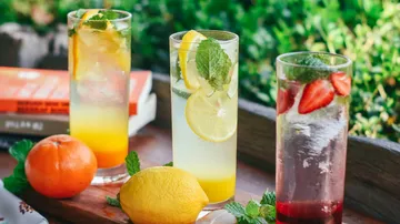 There are three refreshing drinks on a table with fruit.
