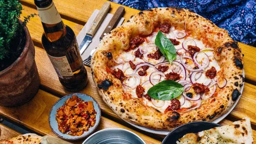 Pizza with toppings served on a wooden table, drinks next to it.