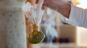 One hand holds a steaming herb packet in the air.