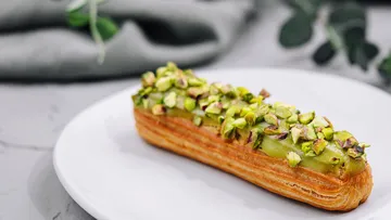 Pistazien-Eclair liegt auf einem weißen Teller.