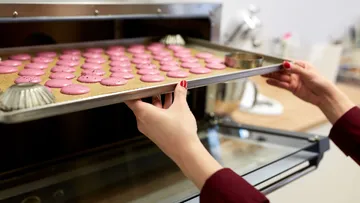 Ein Blech mit rosa Macarons wird aus dem Ofen herausgezogen.