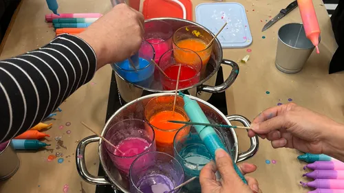 Hands dipping candles into colorful wax.
