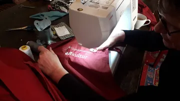 Nähmaschine bearbeitet rote Kleidung auf einem Tisch.
