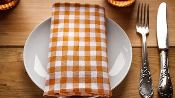 Weißer Teller mit orange-weißem Tischläufer auf Holzuntergrund.
