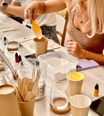 A person mixes materials into a paper cup at the table.