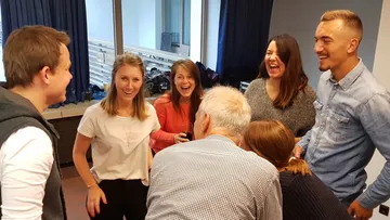 Sechs Personen lachen und unterhalten sich in einem Raum.