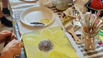 A hand paints a sunflower on a canvas.