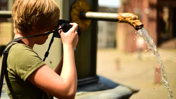 Boy photographs a stream of water from a well.