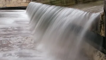 Waterfall flows over a wall into a quiet area.