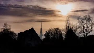 Skyscraper rises behind silhouetted trees and houses.