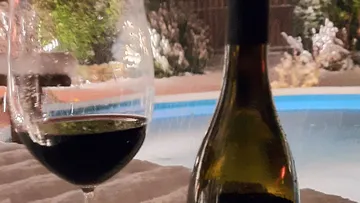 Weinglas und Flasche stehen neben einem Pool bei Nacht.